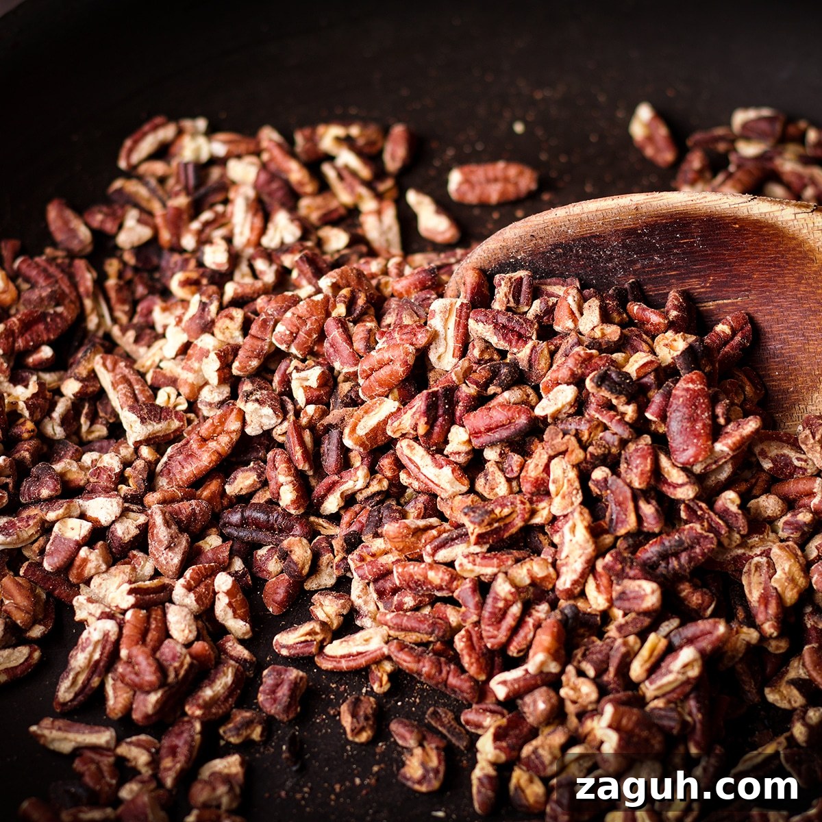 Pecan Pie Made Without Corn Syrup — Classic Recipe with Pure Maple 7 Someone using a wood spoon to stir chopped pecans in a skillet while they toast.