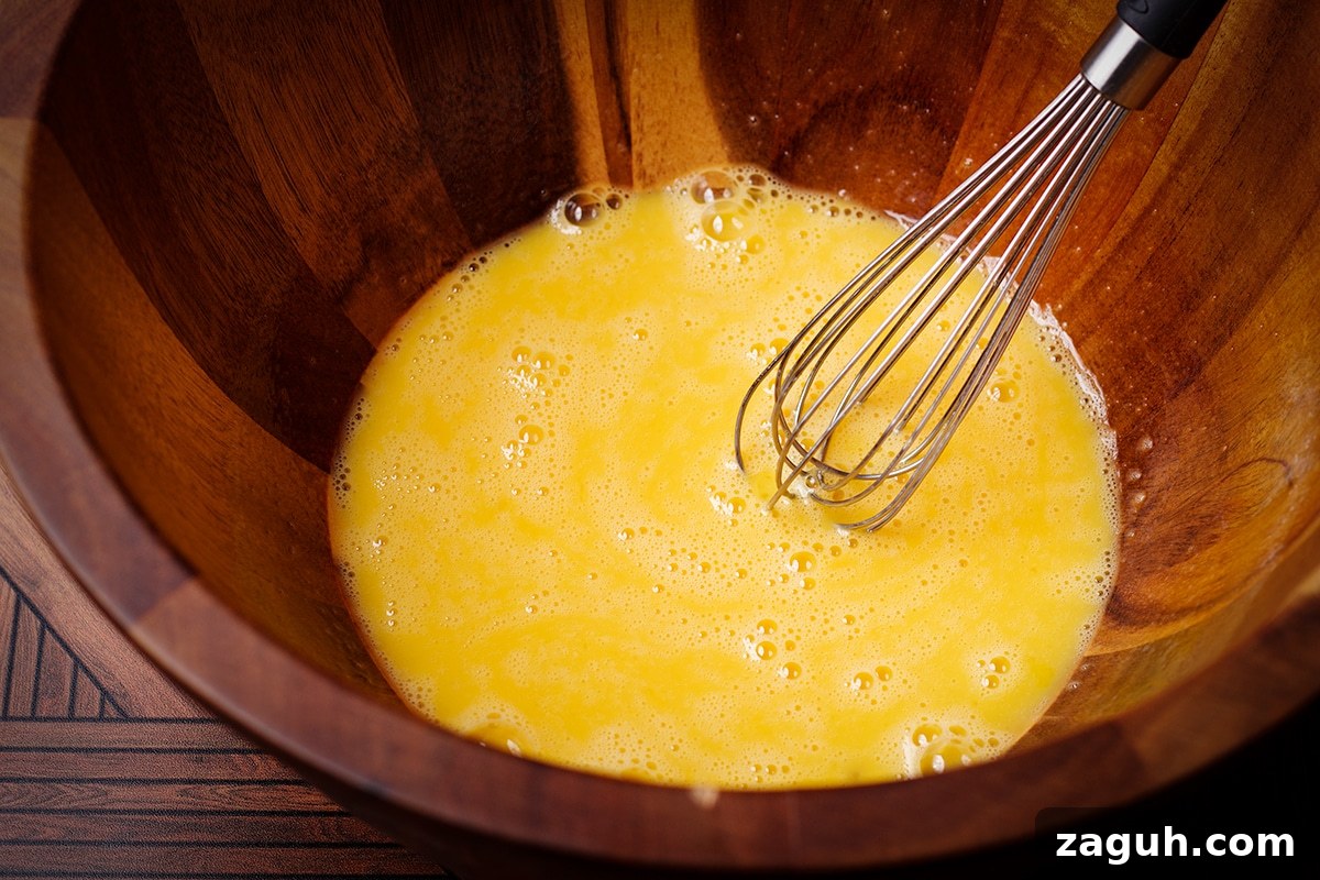 Pecan Pie Made Without Corn Syrup — Classic Recipe with Pure Maple 8 Someone using a wire whisk to beat egg yolks in a wood bowl.