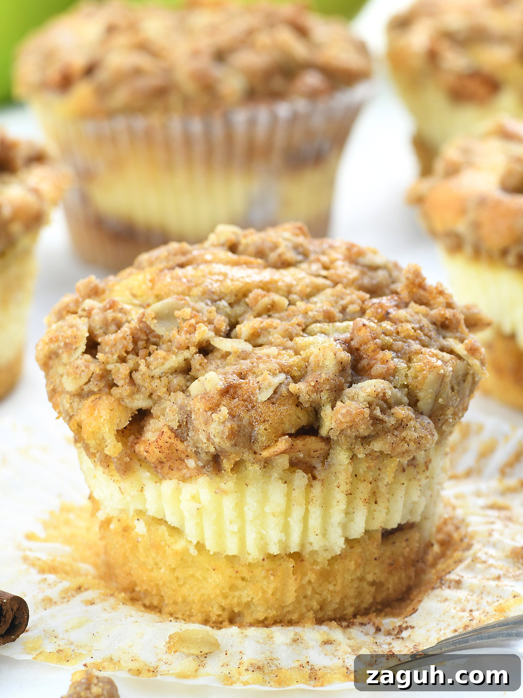 Apple Crisp Cheesecake Muffins with Cinnamon Streusel 3 Apple crisp cheesecake muffin with a golden oat streusel topping and creamy cheesecake layer, displayed in a white cupcake liner with cinnamon sprinkles.