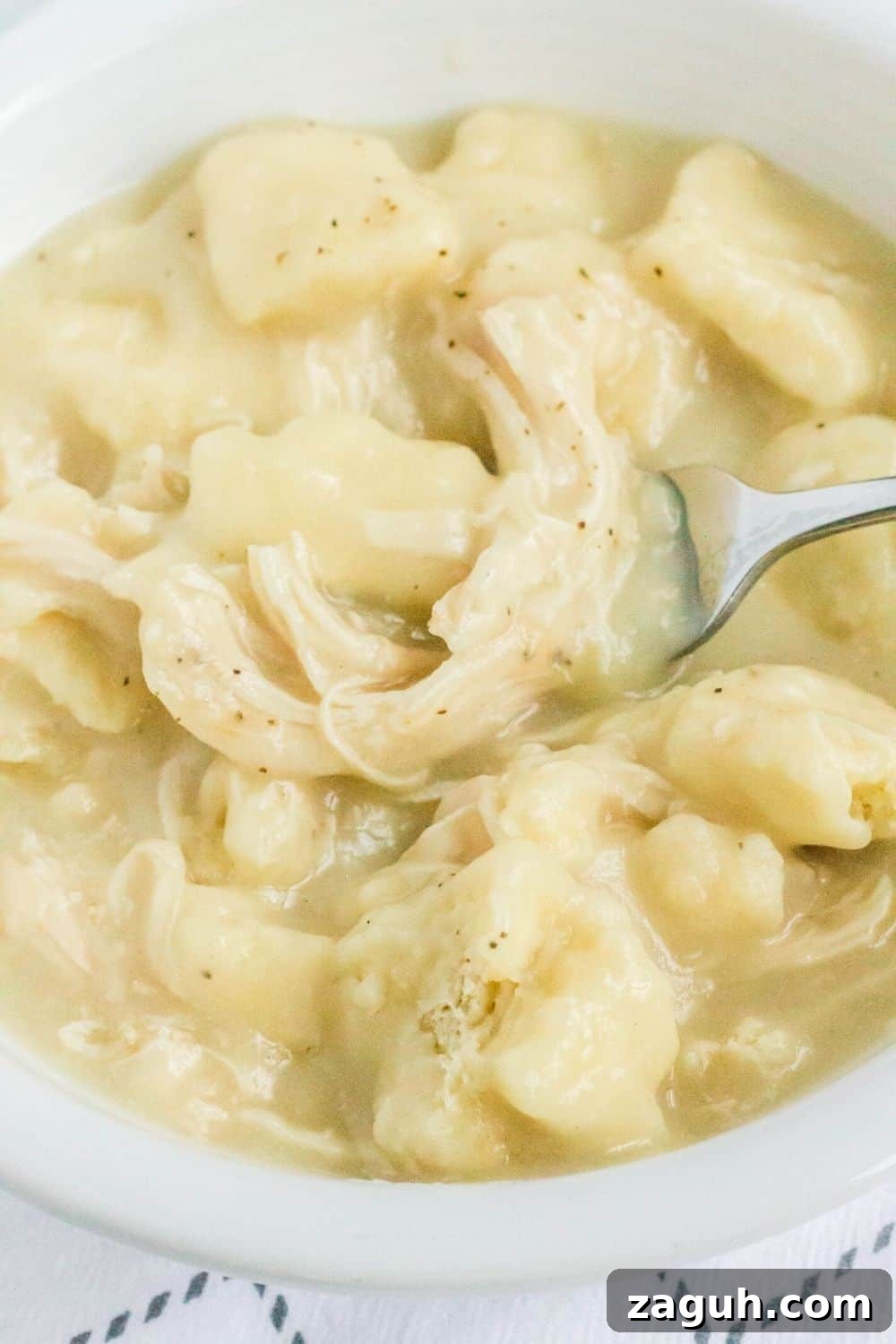 Slow-Cooker Chicken and Dumplings Recipe for Comforting Dinners 11 homemade chicken and dumplings made in the Crock Pot are served in a white bowl. A fork is in the bowl.