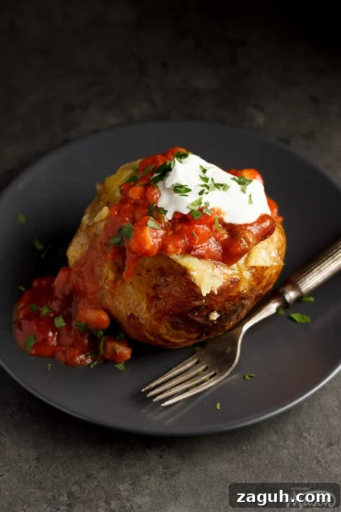 Slow Cooker Jacket Potatoes: Creamy Baked Potatoes Made Ahead 7 A slow cooker jacket potato on a grey plate topped with vegan chilli and vegan creme fraiche
