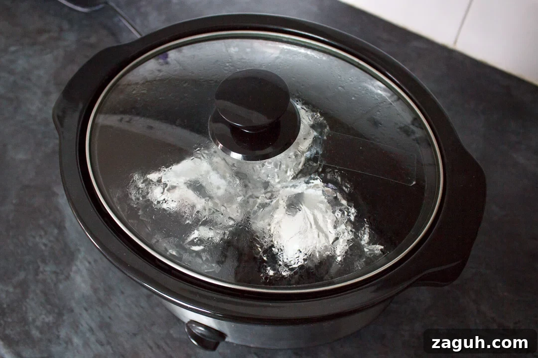 Slow Cooker Jacket Potatoes: Creamy Baked Potatoes Made Ahead 15 jacket potatoes wrapped in foil, cooking in a slow cooker