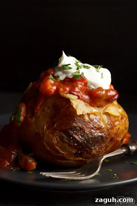 Slow Cooker Jacket Potatoes: Creamy Baked Potatoes Made Ahead 17 A slow cooker jacket potato on a grey plate topped with vegan chilli and vegan creme fraiche