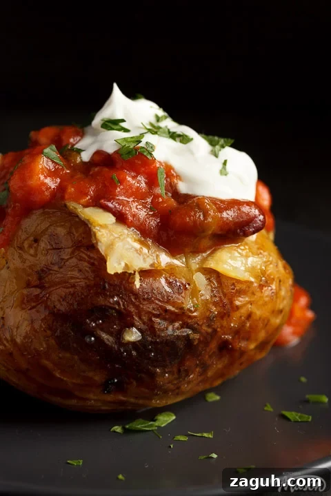 Slow Cooker Jacket Potatoes: Creamy Baked Potatoes Made Ahead 4 A slow cooker jacket potato on a grey plate topped with vegan chilli and vegan creme fraiche