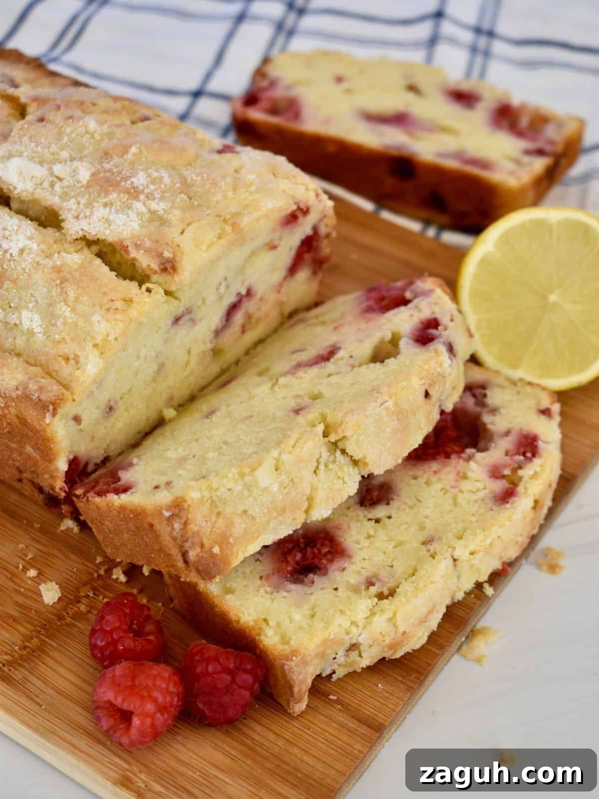Lemon Raspberry Ricotta Loaf Cake Recipe 2 Lemon raspberry loaf cake on a cutting board with raspberries and lemon next to it.