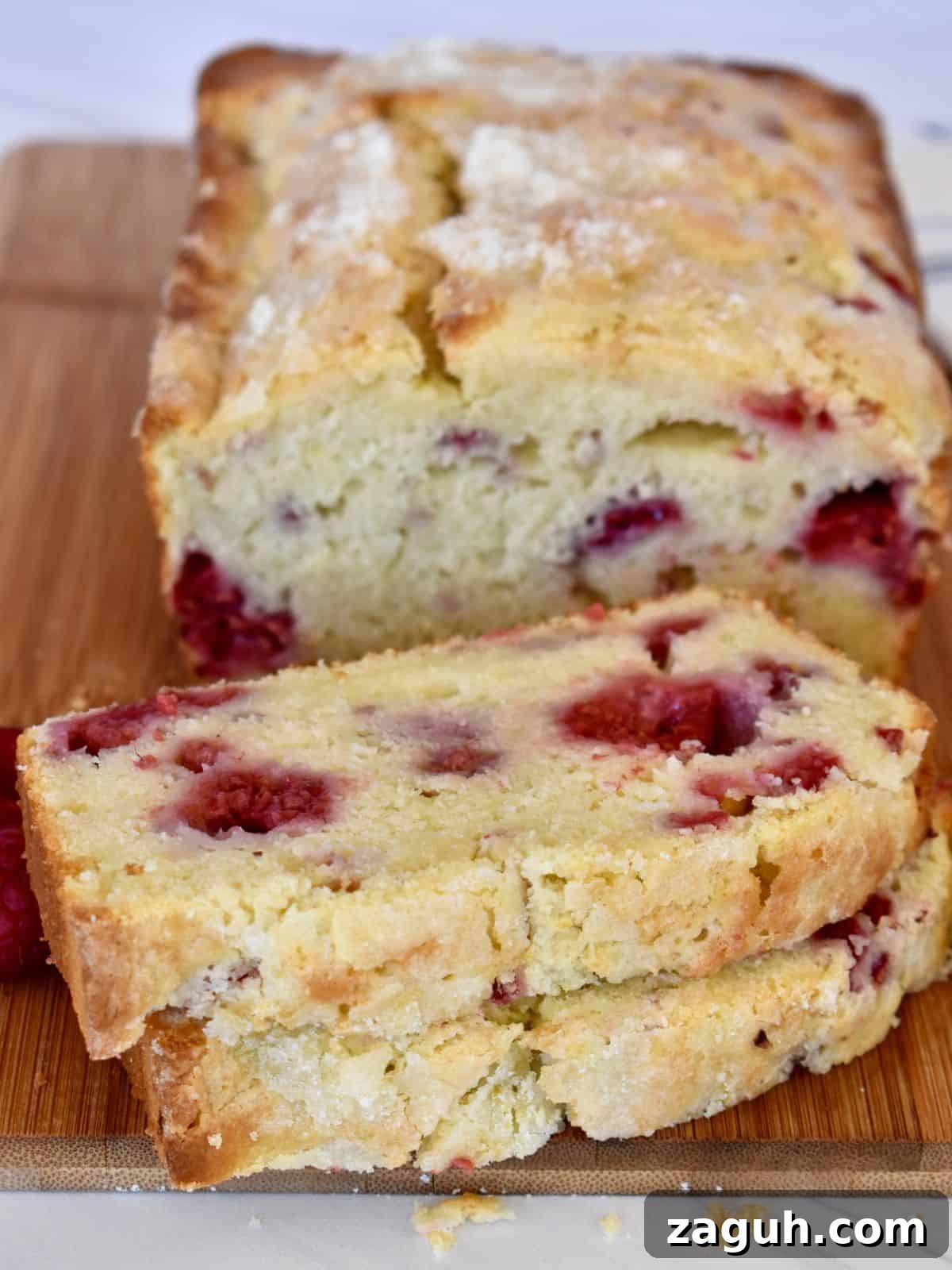 Lemon Raspberry Ricotta Loaf Cake Recipe 8 Sliced lemon raspberry loaf on a wood cutting board with lemon sugar on top.