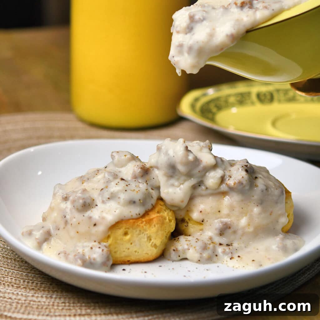 Southern Sausage Gravy Recipe with Biscuits — Classic Comfort Food 6 pouring sausage gravy over biscuits on a white plate
