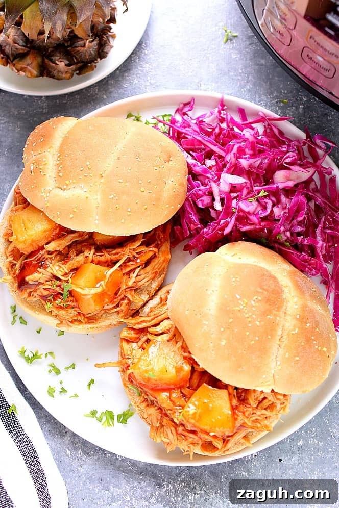 Instant Pot Hawaiian BBQ Chicken Recipe - pulled chicken with sweet pineapple BBQ sauce cooked in pressure cooker. Perfect served as sandwiches! Two sandwiches with pulled BBQ chicken, purple cabbage coleslaw, served on white plate.