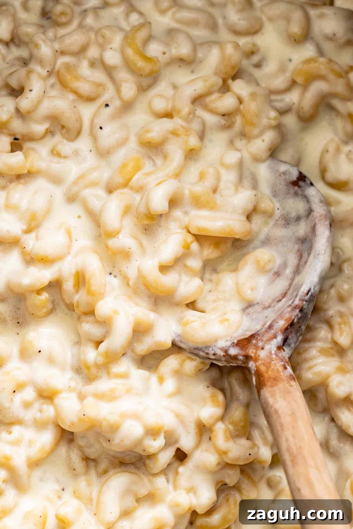 Creamy Slow Cooker Mac and Cheese with Cream Cheese 2 A wood spoon serving a creamy, gooey mac and cheese with white cheese.