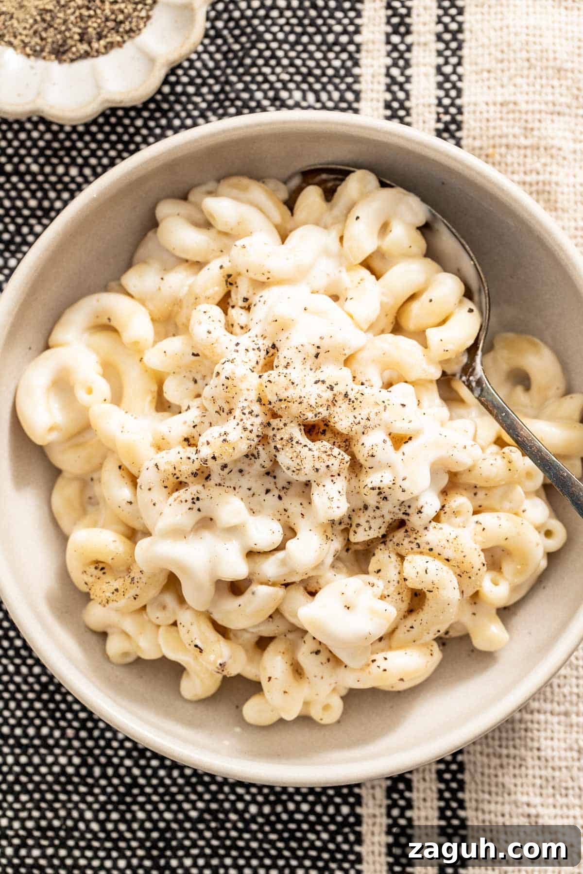 Creamy Slow Cooker Mac and Cheese with Cream Cheese 5 Mac and cheese in a creamy sauce in a white bowl with a spoon and black pepper on top.