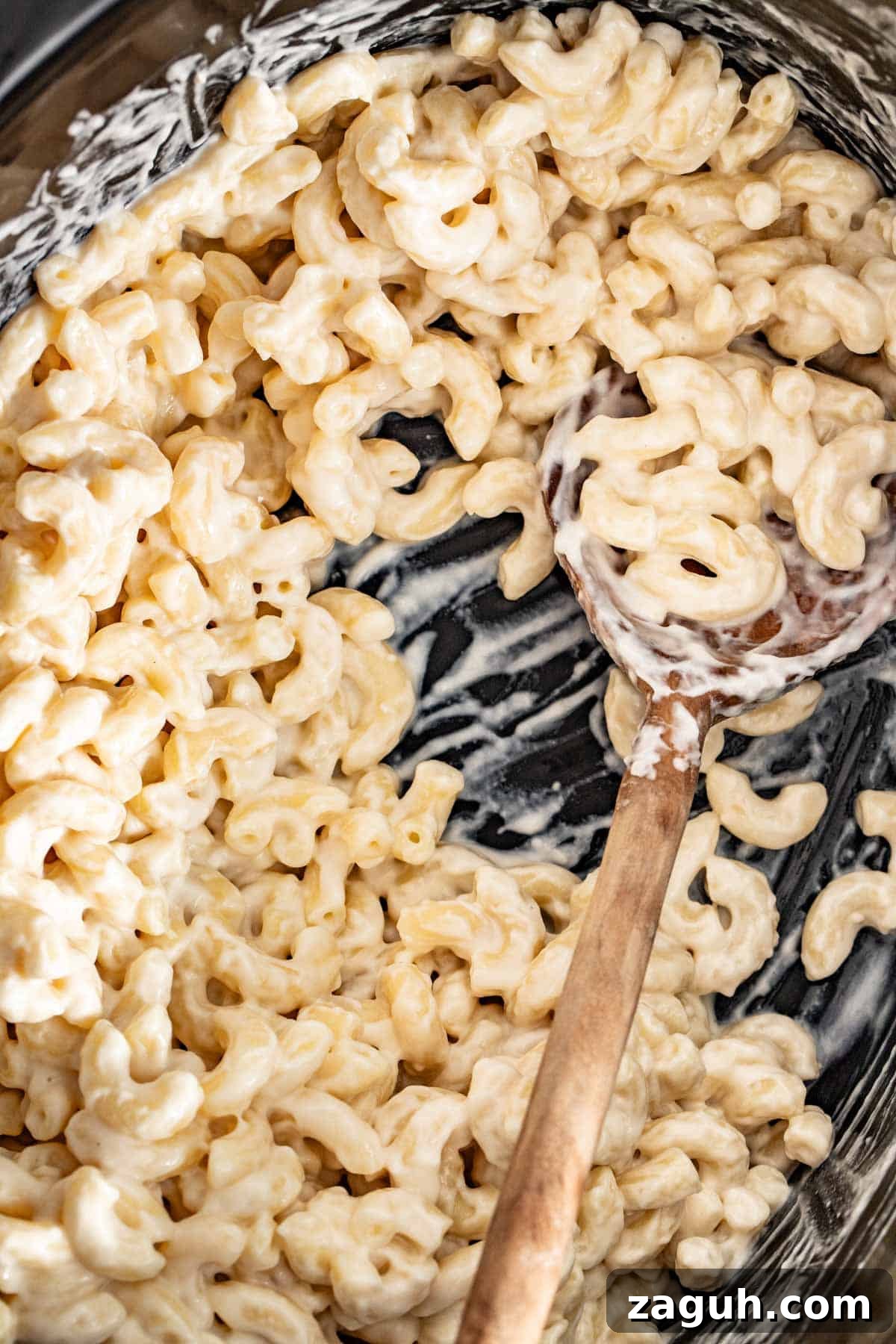 Creamy Slow Cooker Mac and Cheese with Cream Cheese 6 A wood spoon in a slow cooker with mac and cheese and cream cheese on top.