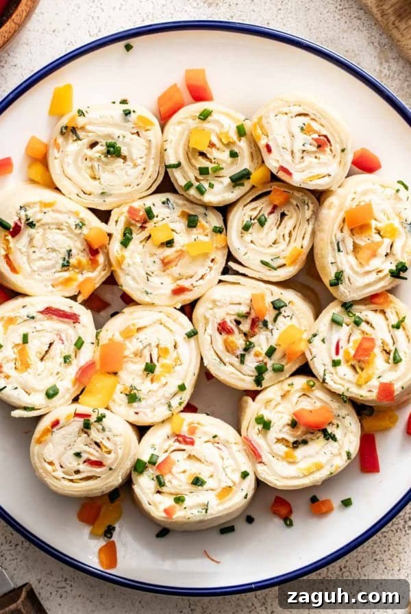 A plate of vegetable tortilla pinwheels with cream cheese and a bowl of peppers next to them.