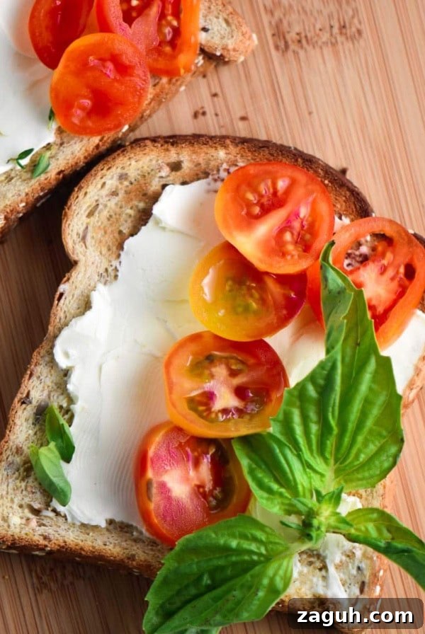 A toast smeared with cream cheese, topped with basil and tomatoes.