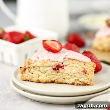 Flaky Strawberry Scones with Glaze — Homemade Recipe 13 A strawberry scone with pink icing and a berry on top on a plate.