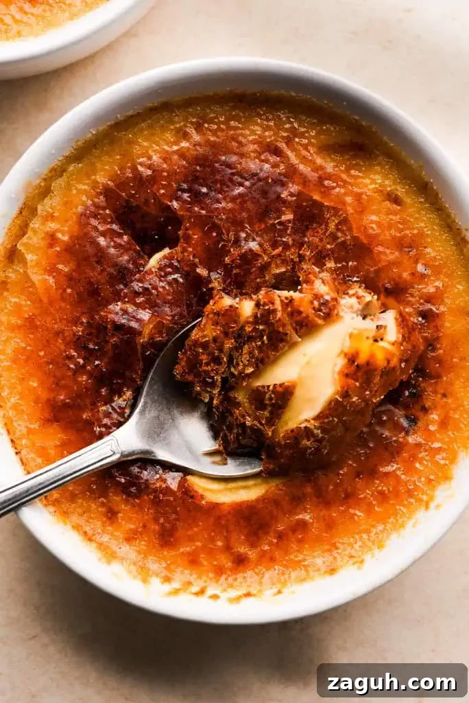 pumpkin spice creme brulee Close-up of a spoon lifting a bite of pumpkin creme brulee, showcasing the creamy texture beneath the crisp caramelized sugar.