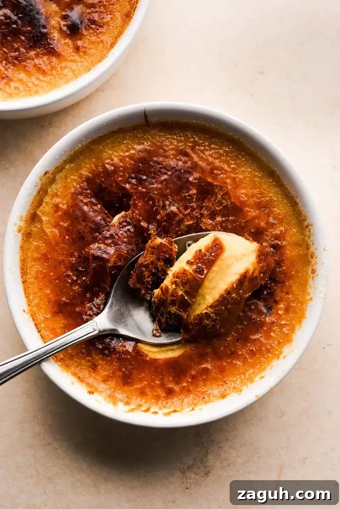 pumpkin creme brulee recipe Spoon breaking into the caramelized top of pumpkin creme brulee, revealing the smooth custard layer below.