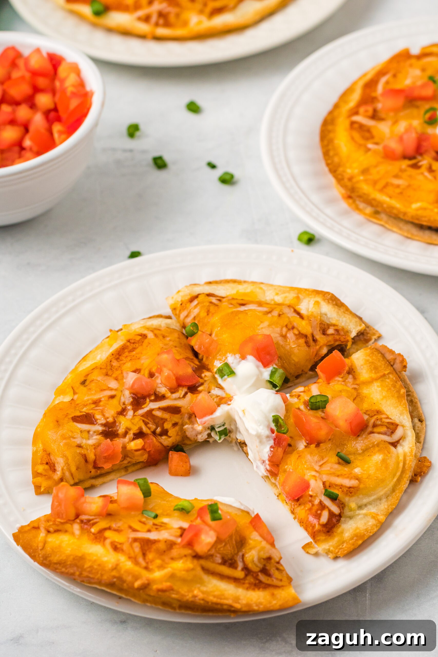 Taco Bell Mexican Pizza: How to Order, Ingredients & Nutrition Facts 2 Mexican Pizza on a white plate cut into quarters topped with sour cream, tomatoes, and green onion.