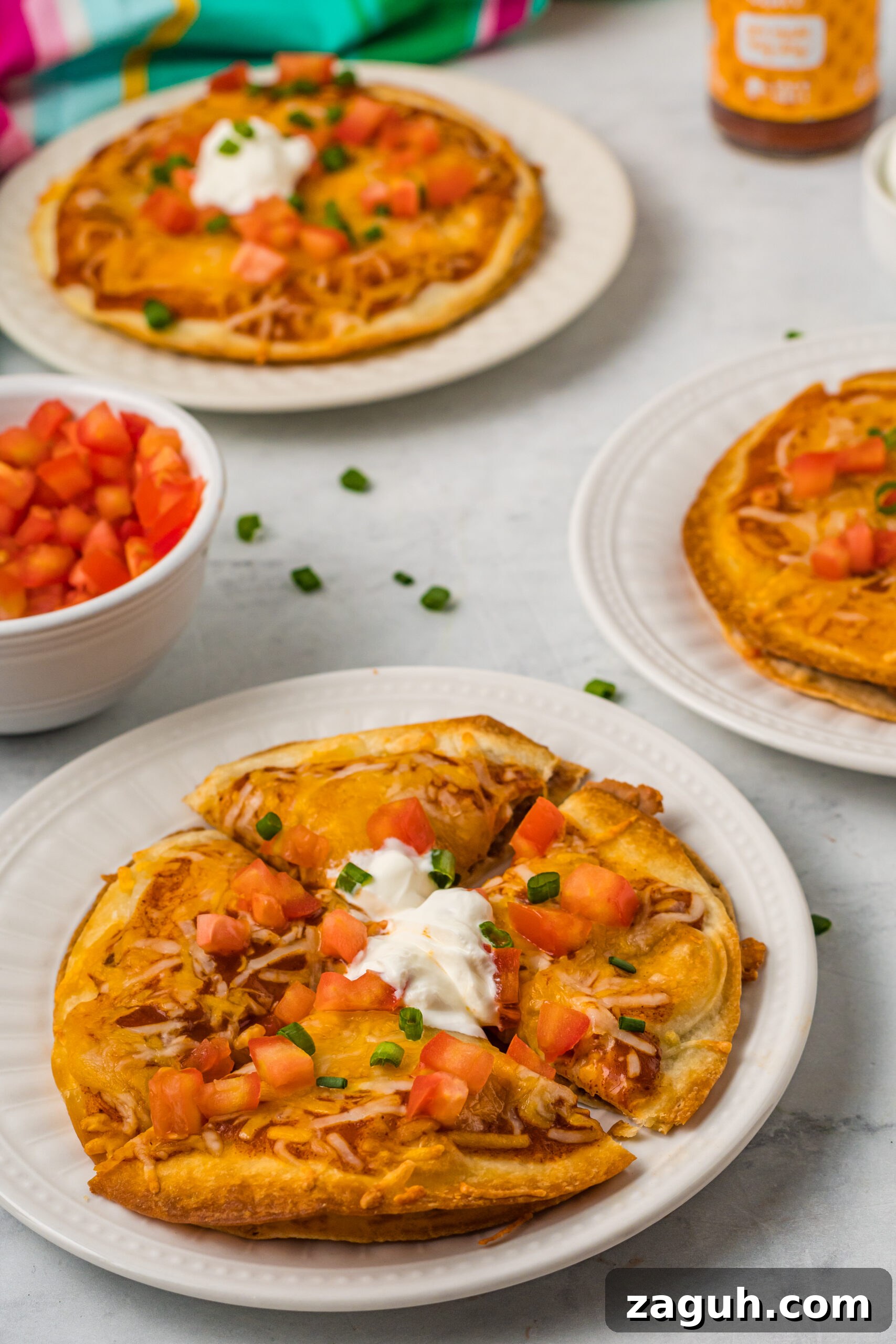 Taco Bell Mexican Pizza: How to Order, Ingredients & Nutrition Facts 4 Mexican Pizza on a white plate cut into quarters topped with sour cream, tomatoes, and green onion.