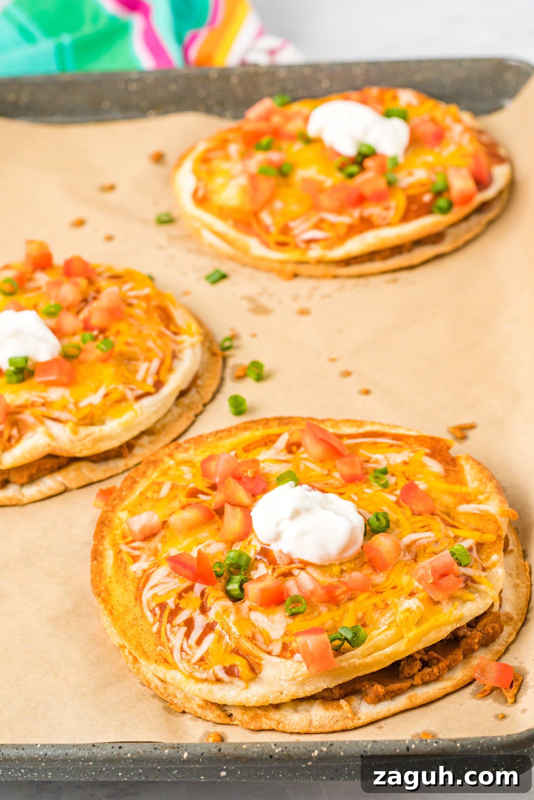 Taco Bell Mexican Pizza: How to Order, Ingredients & Nutrition Facts 8 Mexican Pizzas on a baking sheet topped with sour cream, tomatoes, and green onion.