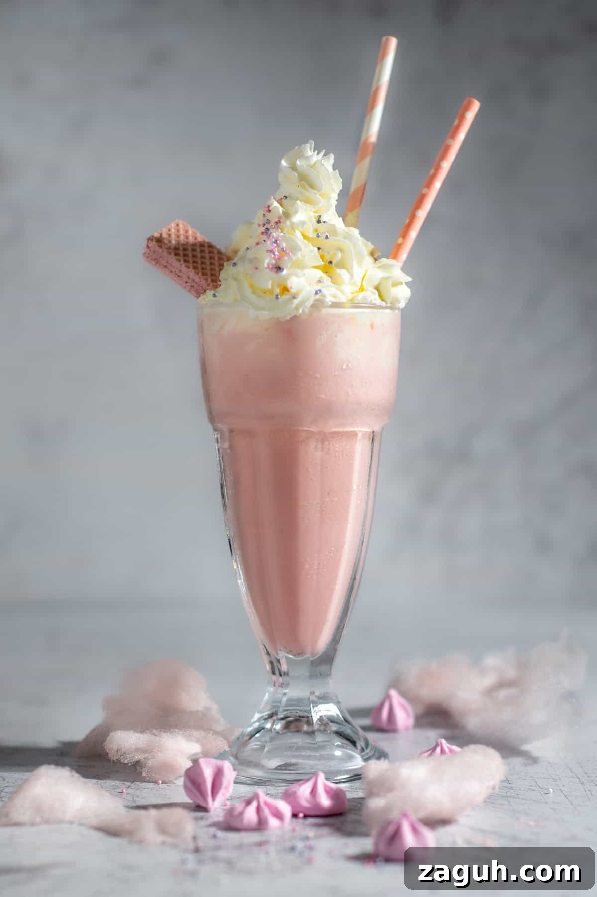 Creamy Strawberry Ice Cream Milkshake with a Secret Twist 2 A large glass of strawberry milkshake with whipped cream in a milkshake glass surrounded by cotton candy.