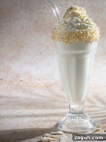 Coconut milkshake in a tall milkshake glass with a glass straw.
