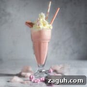 Creamy Strawberry Ice Cream Milkshake with a Secret Twist 9 A large glass of strawberry milkshake with whipped cream in a milkshake glass surrounded by cotton candy.