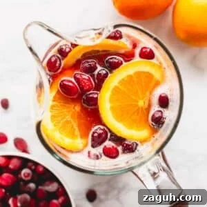 Sparkling Orange Cranberry Spritzer Recipe for Holiday Parties 11 Overhead image of a pitcher of orange cranberry spritzer with pomegranates and orange slices.