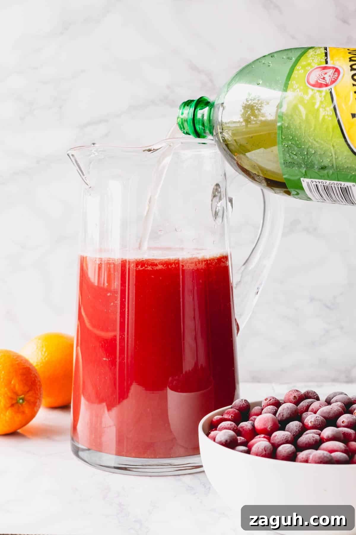 Sparkling Orange Cranberry Spritzer Recipe for Holiday Parties 6 Ginger ale being poured into a pitcher of orange juice and cranberry juice.