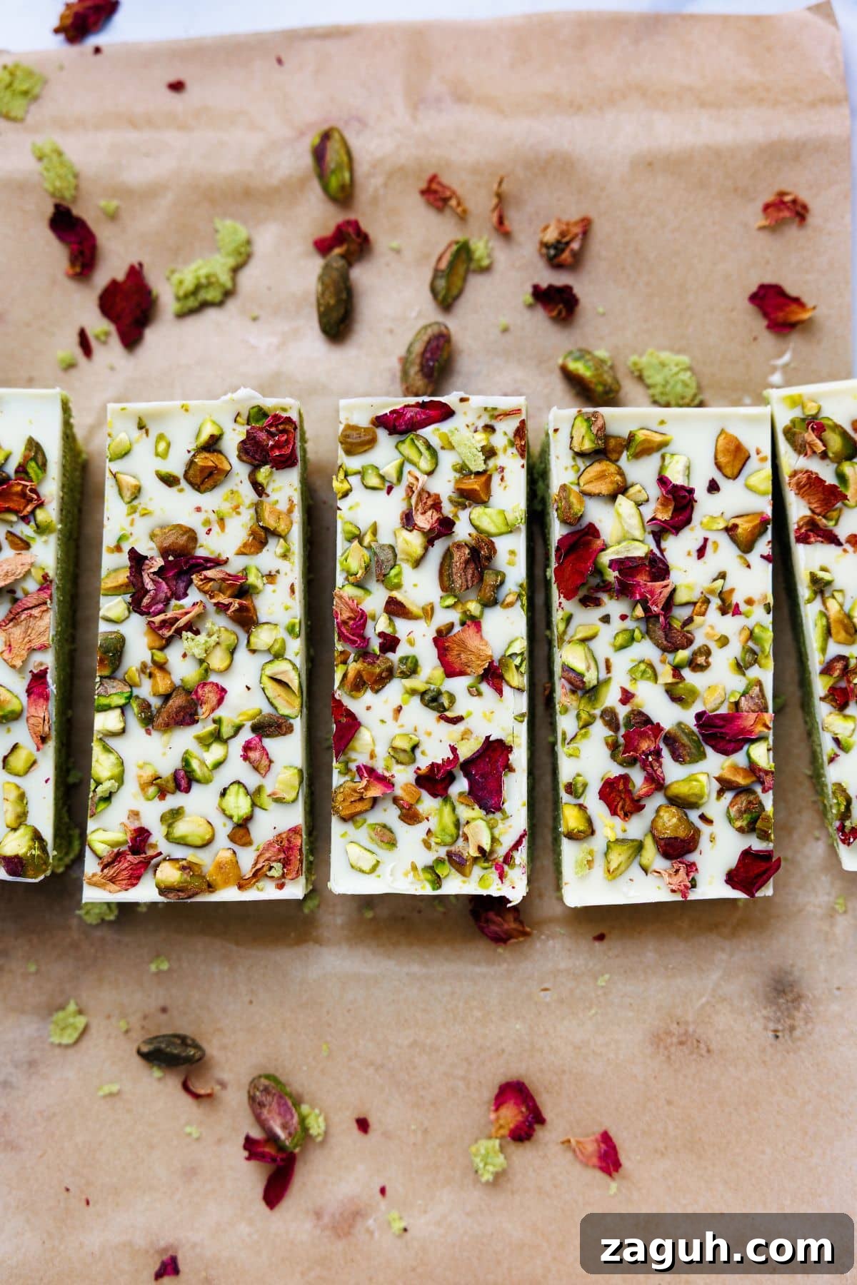 Homemade Pistachio Protein Bars Recipe for High-Energy Snacks 11 Four pistachio protein bars arranged in row on parchment paper, showing white chocolate tops decorated with pistachios and rose petals