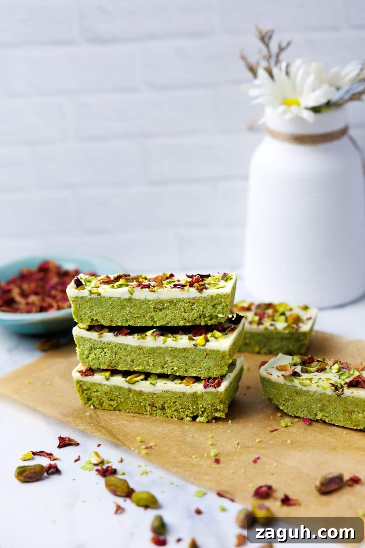Homemade Pistachio Protein Bars Recipe for High-Energy Snacks 12 Stack of three pistachio protein bars on parchment paper with white ceramic vase and daisies in soft-focused background