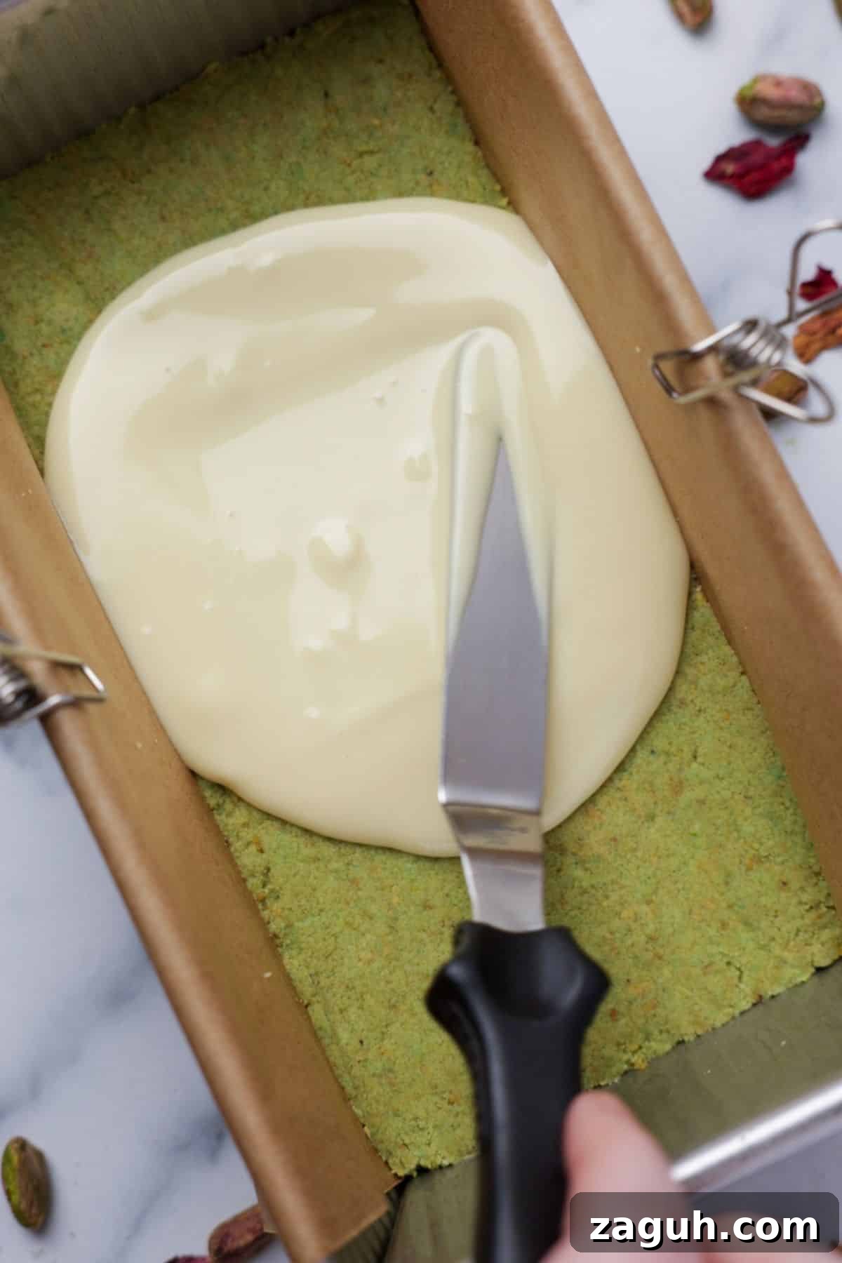 Homemade Pistachio Protein Bars Recipe for High-Energy Snacks 7 Melted white chocolate being spread over pistachio base in loaf pan using offset spatula