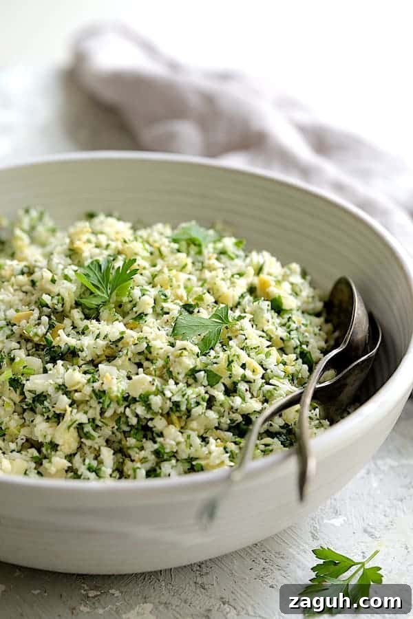 Cauliflower & Artichoke Tabbouleh: Fresh Low-Carb Salad Recipe 6 Close-up photo of Cauliflower Artichoke Tabbouleh in white bowl with serving utensils garnished with parsley.