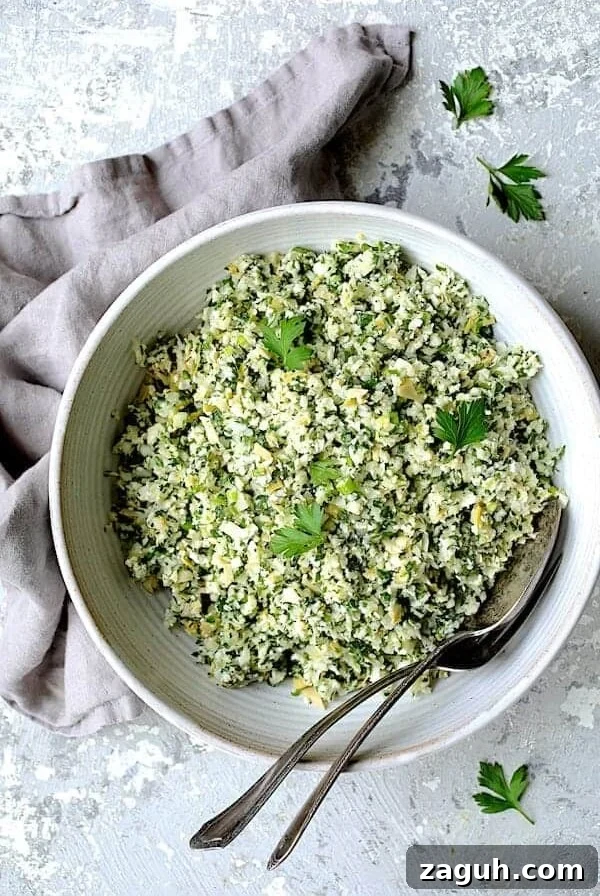 Cauliflower Artichoke Tabbouleh in white serving bowl with serving utensils garnished with fresh parsley.