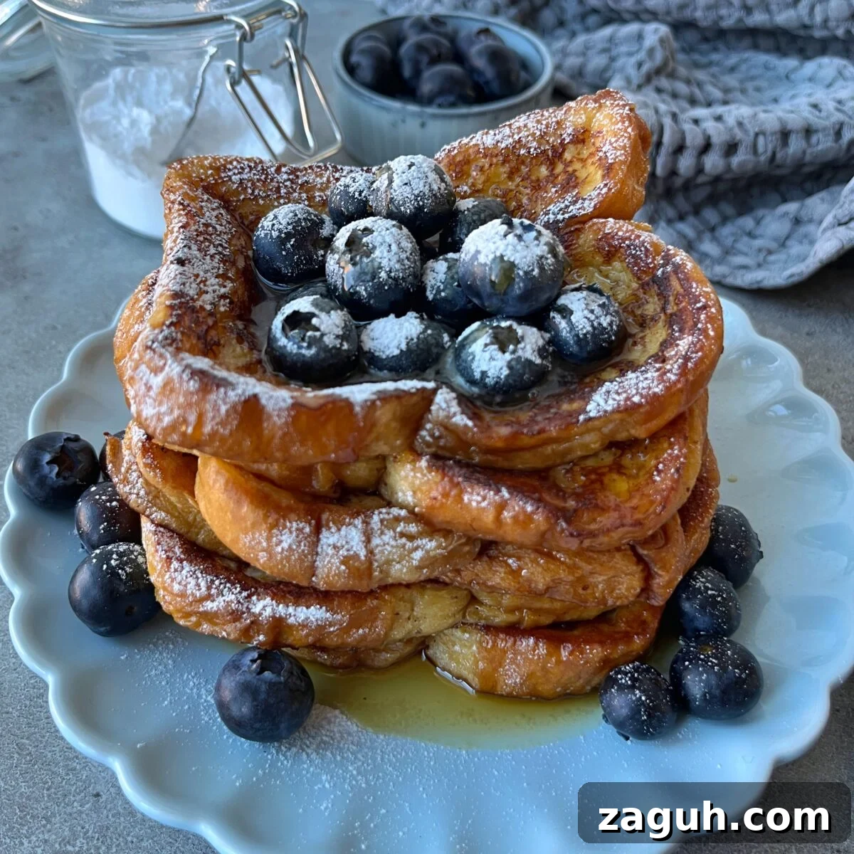 Decadent Brioche French Toast Recipe for Brunch and Dessert 2 A stack of Brioche French Toast topped with fresh blueberries and powdered sugar, served on a white plate with extra blueberries and syrup.