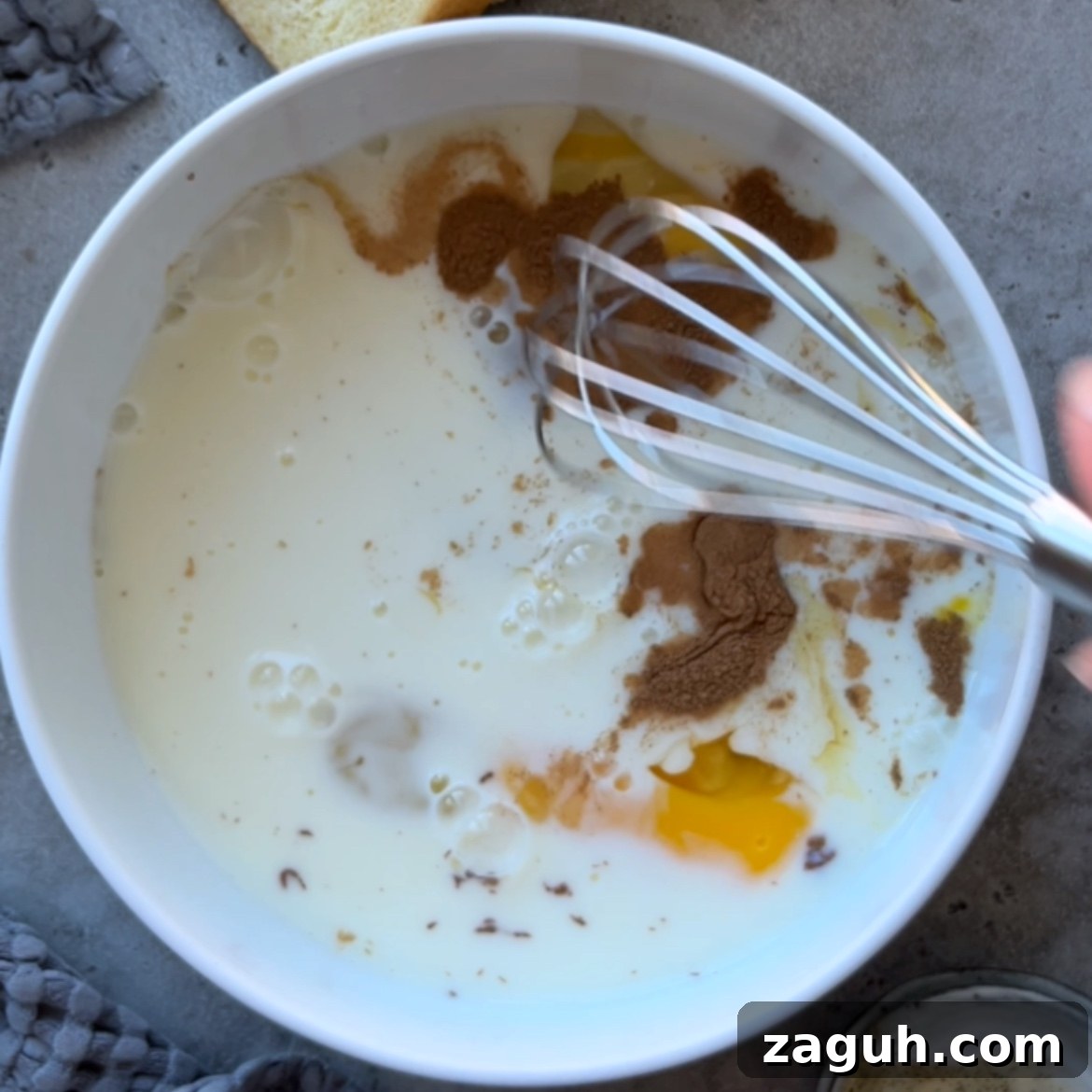 Decadent Brioche French Toast Recipe for Brunch and Dessert 5 A whisk stirring eggs, milk, and spices in a white bowl, preparing a delicious mixture for Brioche French Toast.