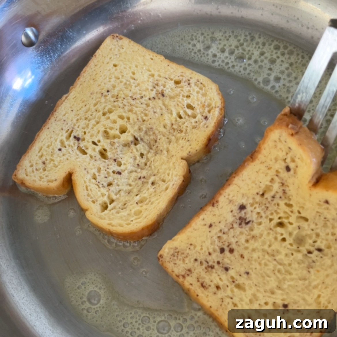 Decadent Brioche French Toast Recipe for Brunch and Dessert 7 Two slices of Brioche French Toast coated in egg mixture are frying in a stainless steel pan, with a spatula lifting one slice.