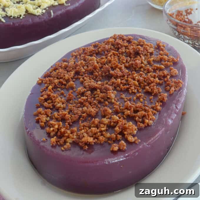 Ube Halaya Recipe: How to Make Creamy Filipino Purple Yam Dessert 6 ube halaya topped with latik on a white serving platter with a ube halaya topped with cheese in the background.