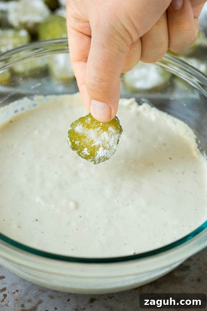 Dipping Pickle Slice A slice being dipped into a bowl of beer batter.