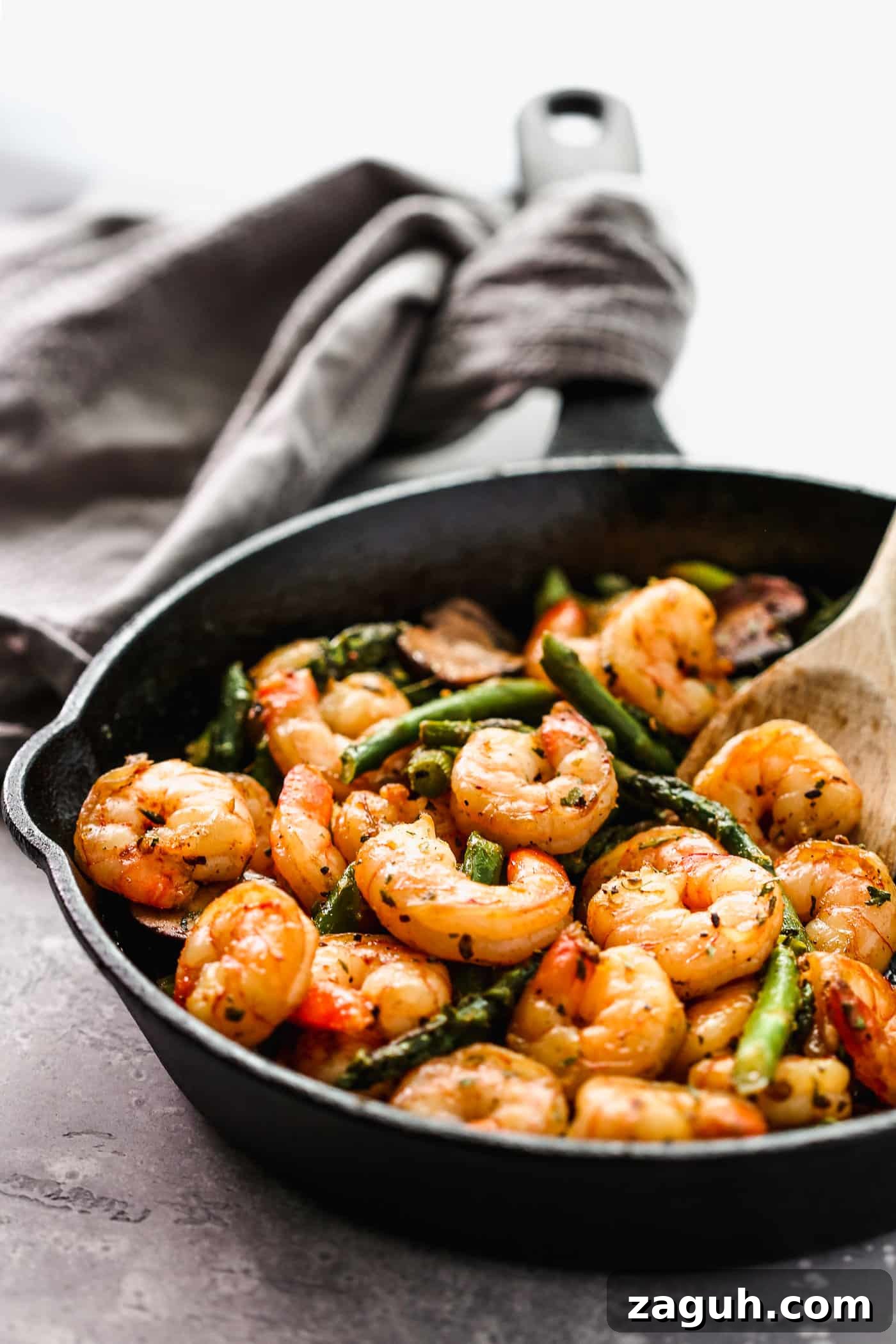 15 Whole30 Meal-Prep Recipes for Stress-Free Weekly Planning 12 Shrimp and asparagus in a cast iron skillet with a wooden spoon on the side.