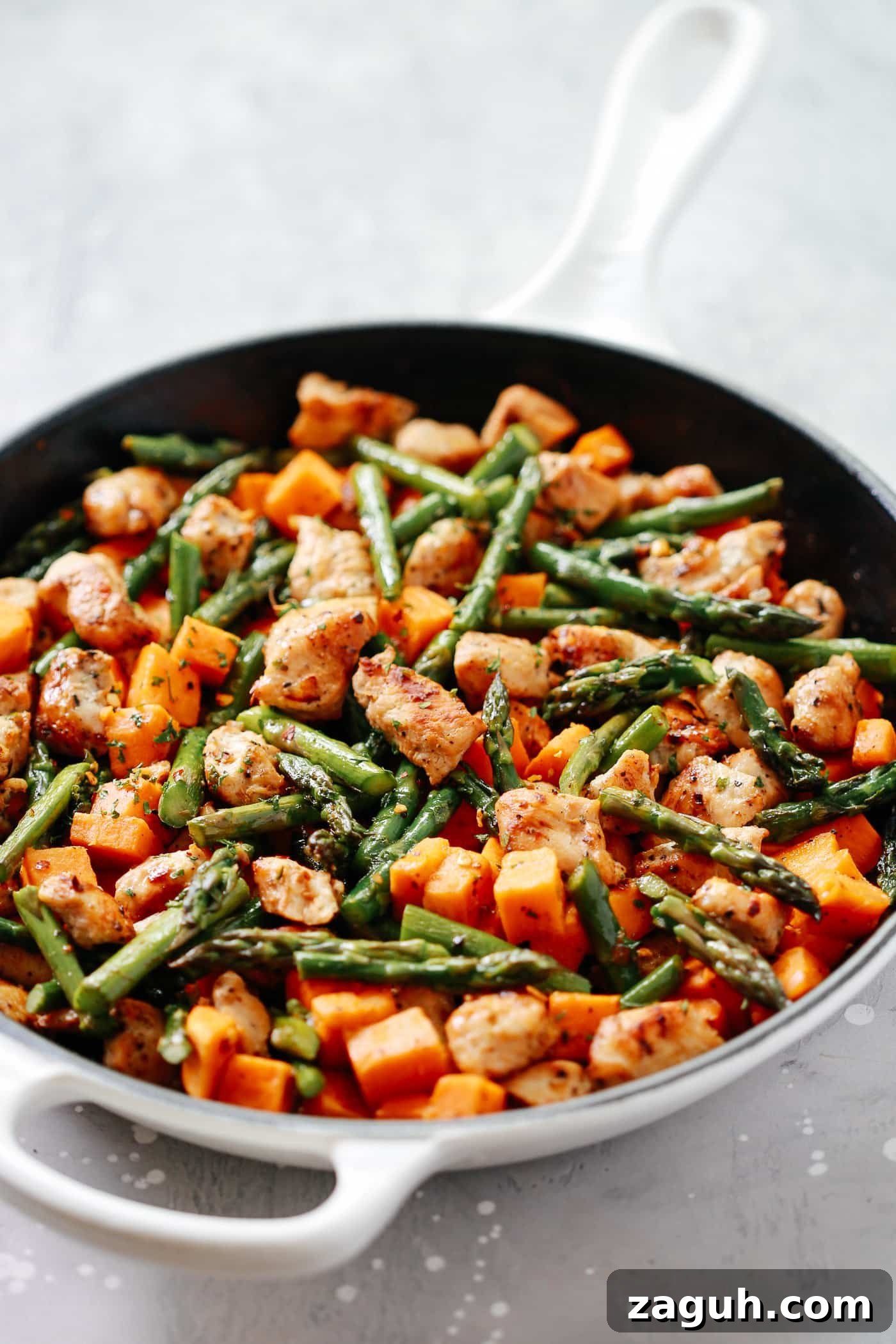 15 Whole30 Meal-Prep Recipes for Stress-Free Weekly Planning 9 A white skillet containing chicken, asparagus, and sweet potatoes with herbs on top.
