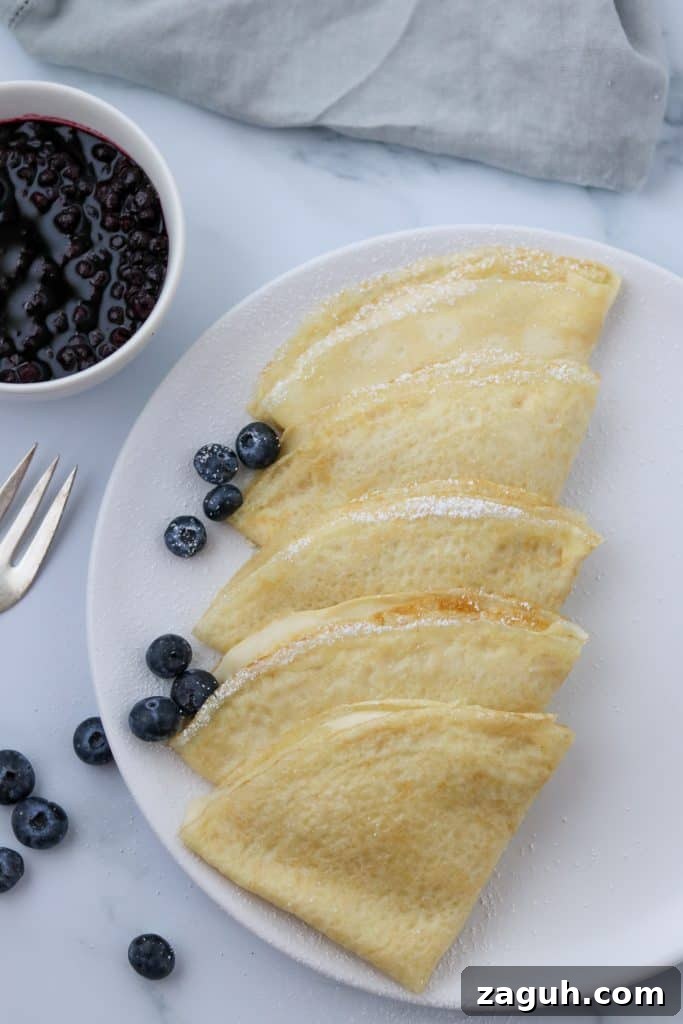 Swedish Pancakes with Vanilla Pastry Cream & Blueberry-Cardamom Compote 2 A plate of Swedish pancakes with blueberries and a fork