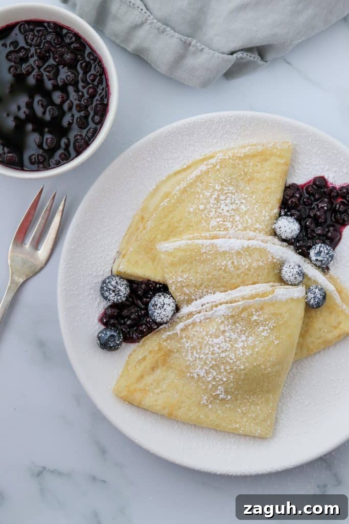 Swedish Pancakes with Vanilla Pastry Cream & Blueberry-Cardamom Compote 3 A plate of Swedish pancakes with blueberries and a fork