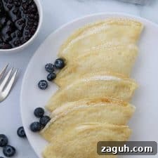 A plate of Swedish pancakes with blueberries and a fork
