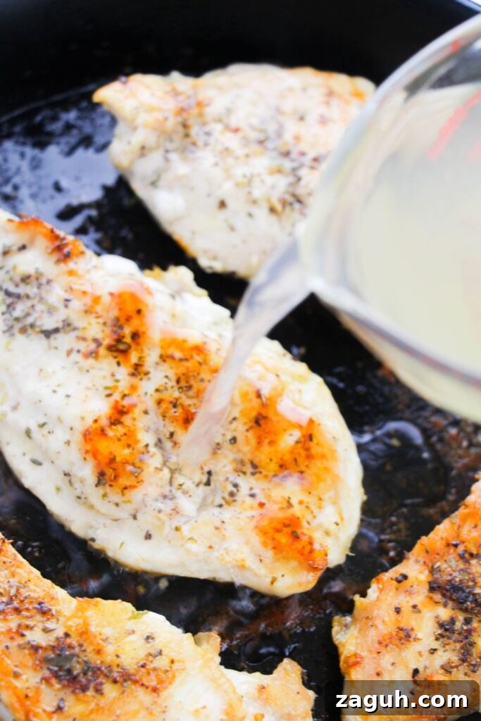 Tuscan-Style Creamy Garlic Chicken with Sun-Dried Tomatoes 6 pouring broth over seared chicken that is in a cast iron skillet