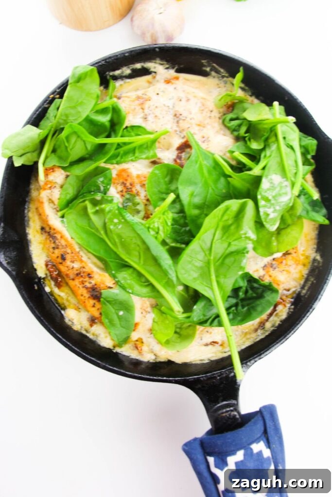 Tuscan-Style Creamy Garlic Chicken with Sun-Dried Tomatoes 9 fresh spinach on top of chicken and broth in a cast iron skillet
