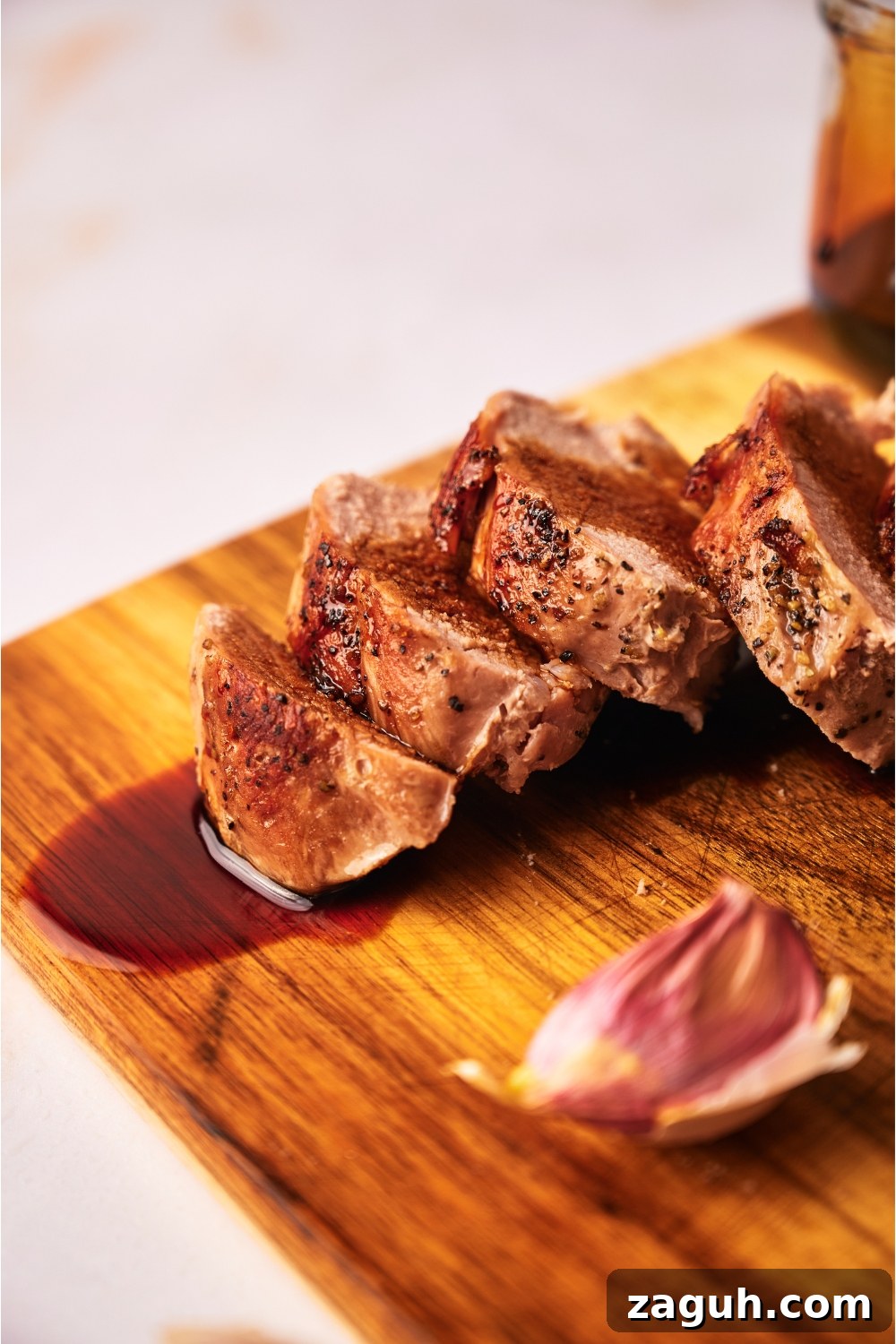Juicy Sous Vide Pork Tenderloin Recipe — Perfectly Cooked Every Time 11 Close up of cooked pork tenderloin coated in a brown sauce atop a wood cutting board.