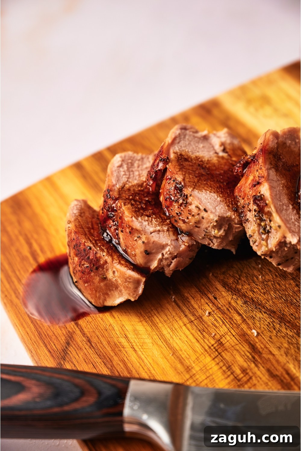 Juicy Sous Vide Pork Tenderloin Recipe — Perfectly Cooked Every Time 12 Close up of cooked pork tenderloin coated in a brown sauce atop a wood cutting board.