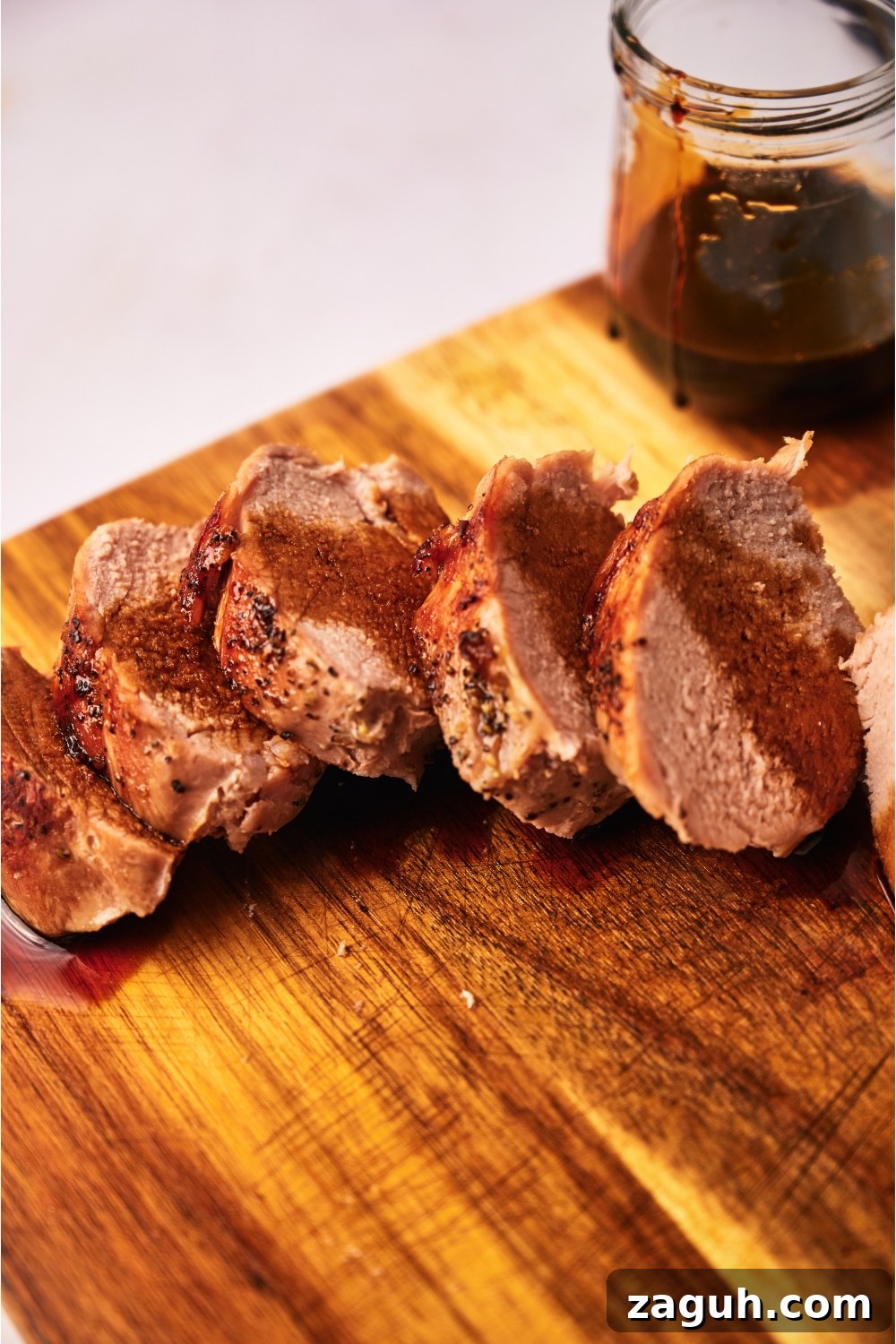 Juicy Sous Vide Pork Tenderloin Recipe — Perfectly Cooked Every Time 13 Close up of cooked pork tenderloin coated in a brown sauce atop a wood cutting board.