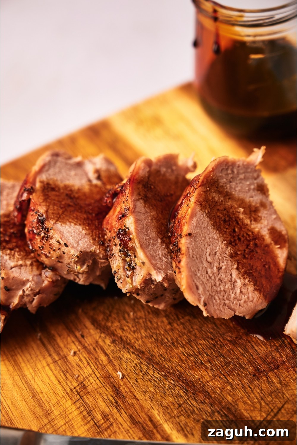 Juicy Sous Vide Pork Tenderloin Recipe — Perfectly Cooked Every Time 3 Close up of cooked pork tenderloin coated in a brown sauce atop a wood cutting board.