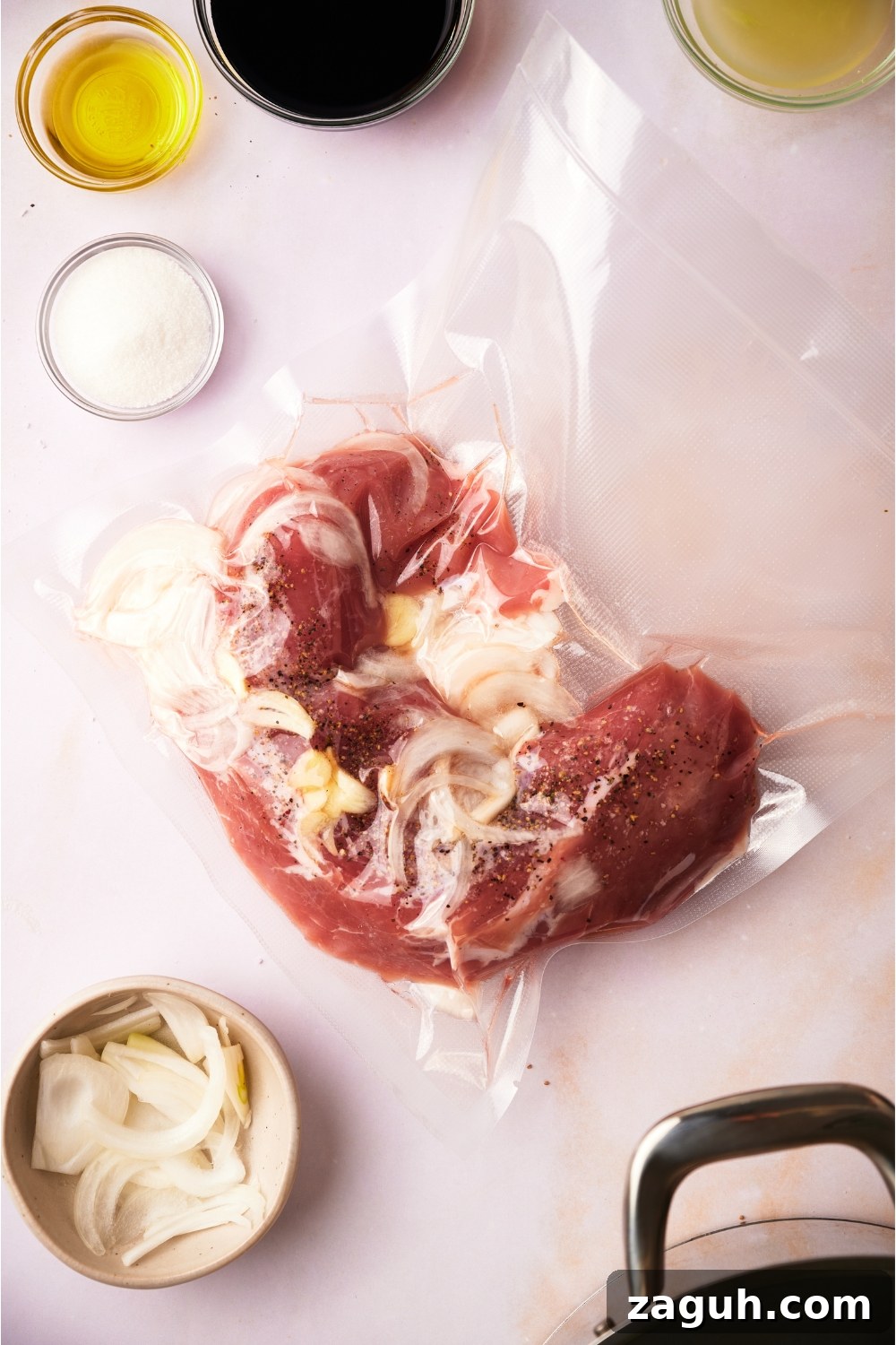 Juicy Sous Vide Pork Tenderloin Recipe — Perfectly Cooked Every Time 5 Pork tenderloin vacuum sealed with garlic and onion, surrounded by an assortment of ingredients.
